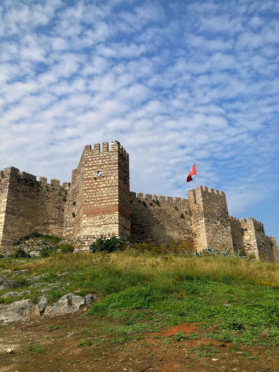 The stone and brick towers of Ayasuluk Fortress on the hill above Selçuk, with a Turkish flag flying from the walls