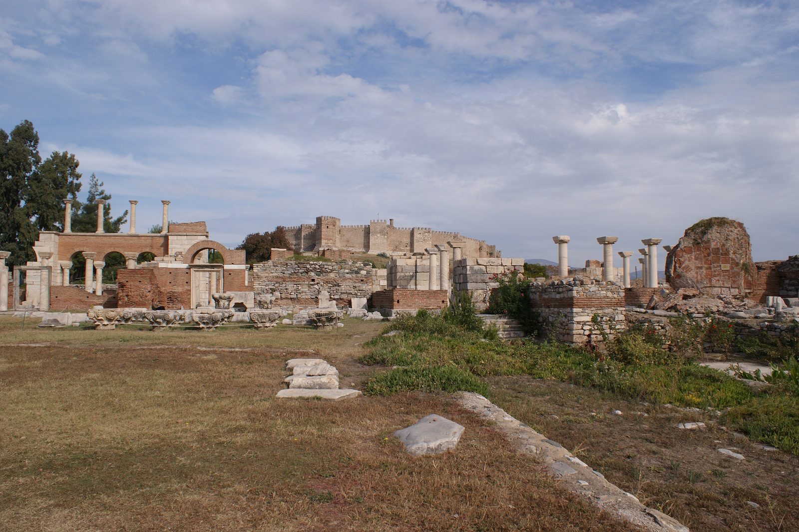 The brick arches and re-erected marble columns of the Basilica of St John in Selçuk, with the walls and towers of Ayasuluk Fortress on the hill behind
