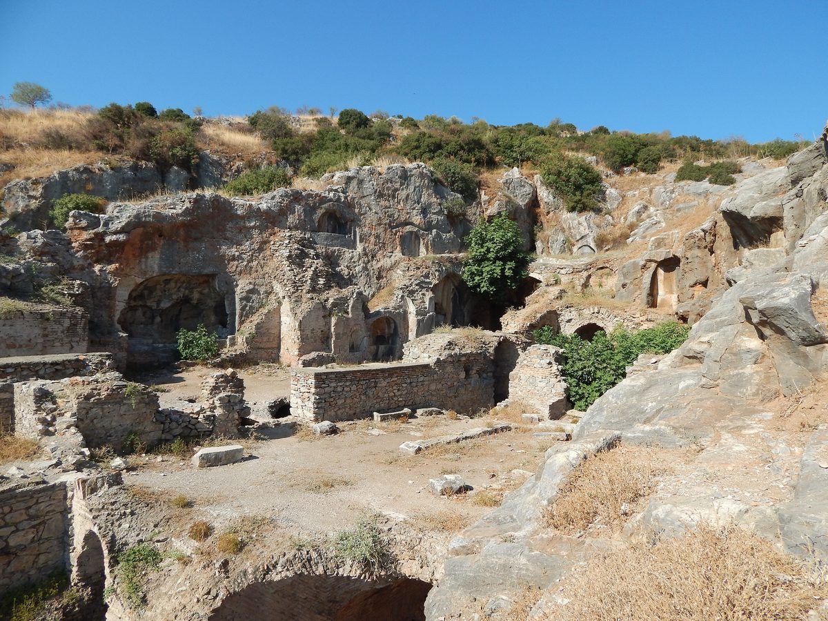 The rock-cut chambers and stone walls of the Cave of the Seven Sleepers on the slope of Panayır Hill at Ephesus, under a blue sky