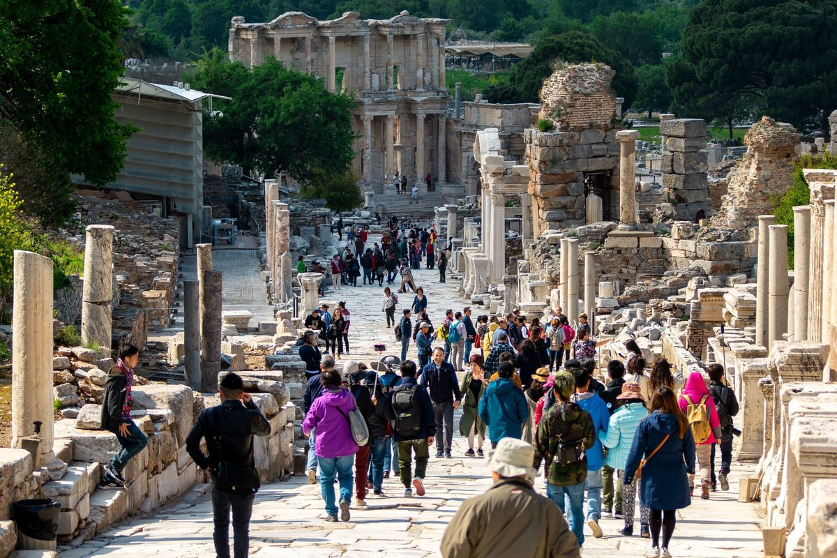 Visitors in jackets, long pants and walking shoes on the pale marble paving of Curetes Street in spring, with the Library of Celsus at the far end