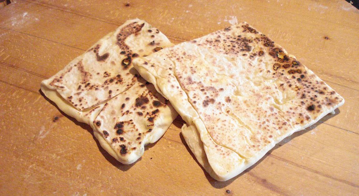 Two folded gözleme flatbreads, browned in spots from the griddle, on a floury wooden board