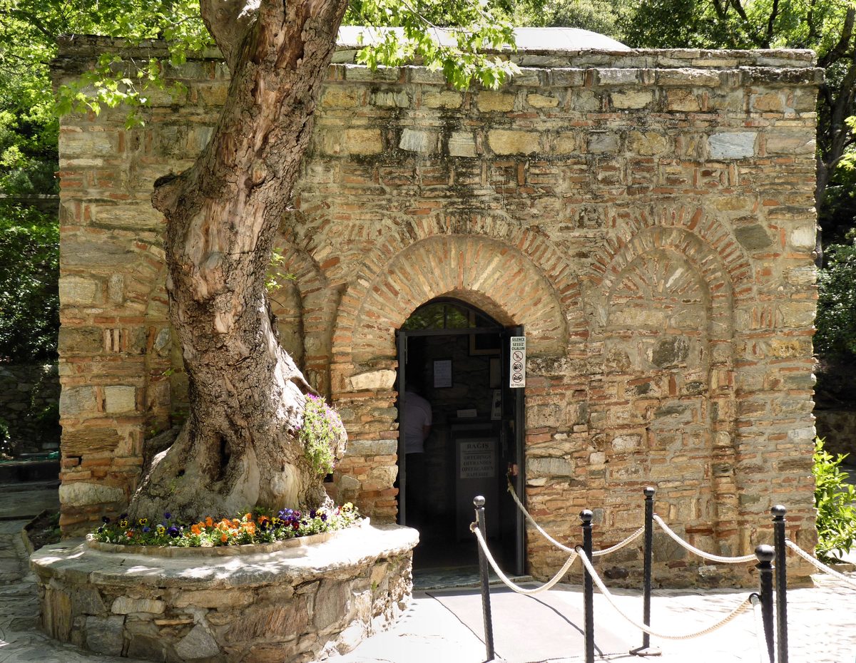 The stone and brick chapel of the House of the Virgin Mary with its door open, a sign beside it reading Silence, Sessiz Olalım and No Photos, and rope barriers for the line in front