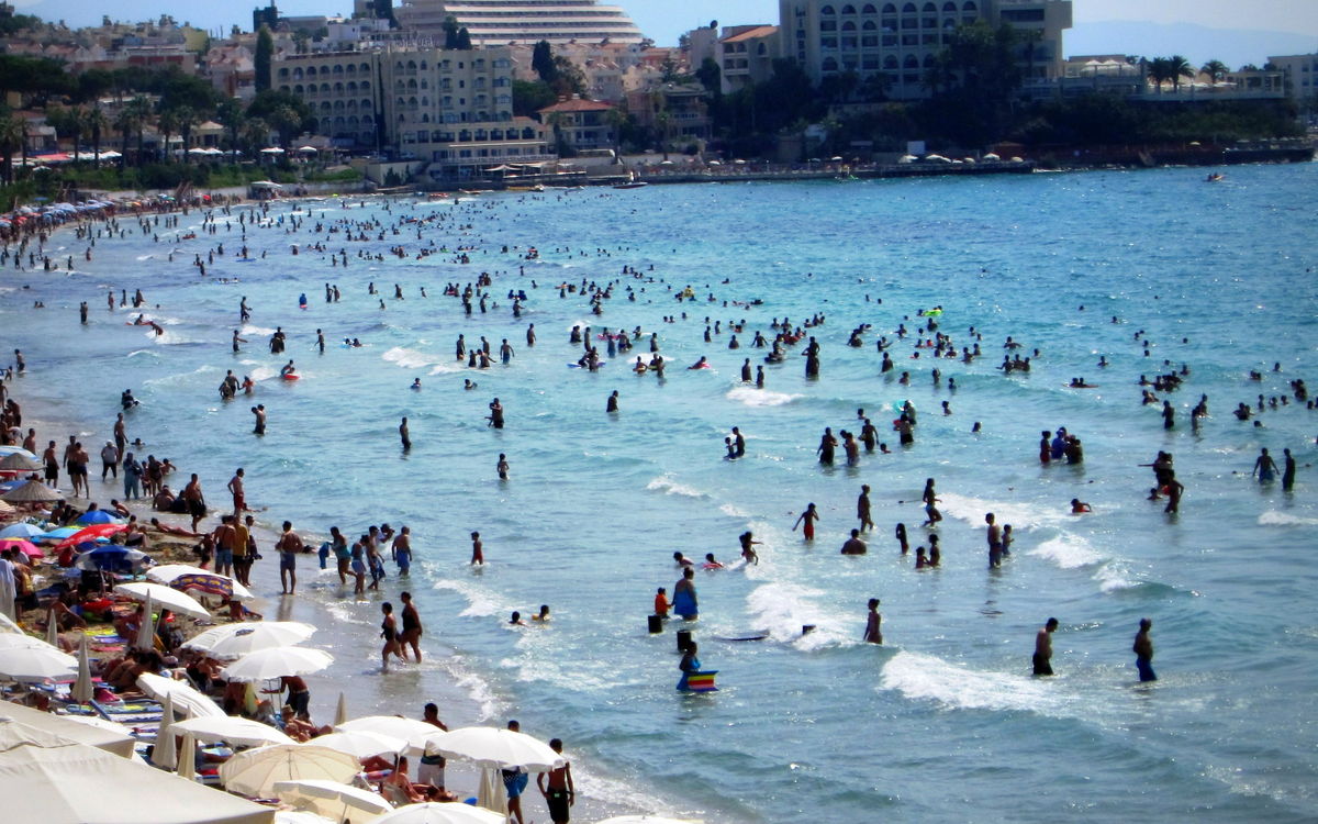 Swimmers in the shallow water and rows of parasols along the sand at Ladies Beach in Kuşadası
