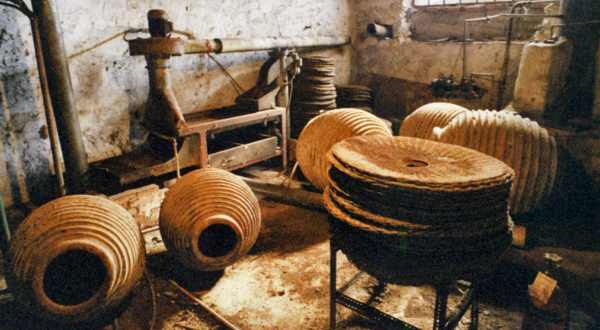 An old olive press room with an iron press against the wall and stacks of round woven press mats on the floor