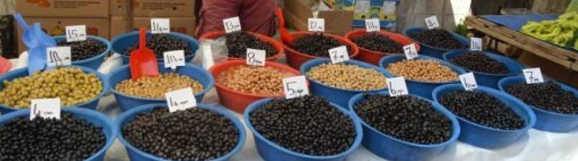 Rows of blue and red tubs of black and green olives on a market table, each with a small handwritten price card